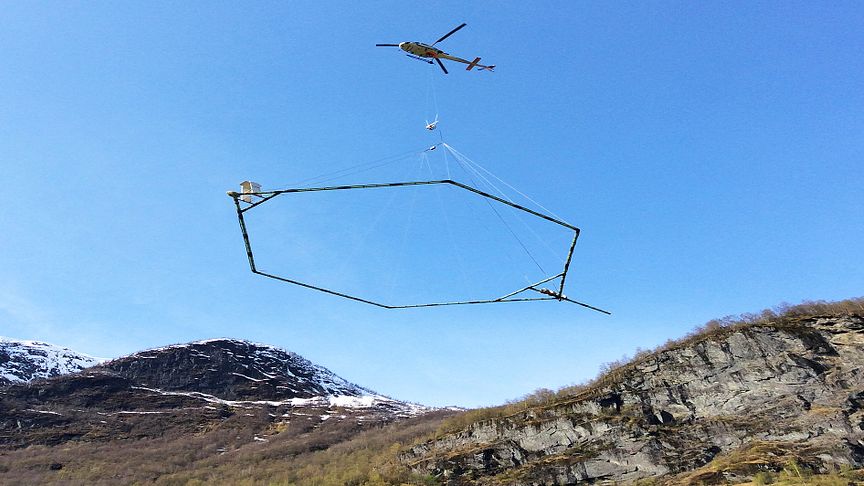 Antennen som registrerer grunnforholdene henger under helikopteret som kjører over områdene som ønskes undersøkt.