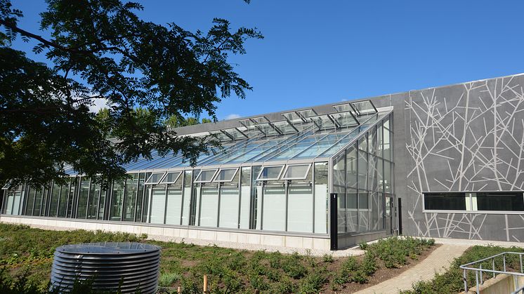 Den nya byggnaden i betong med inslag av grafiskt mönster i fasaden och ett stort växthus i glas ger forskningsanläggningen en egen karaktär i samklang med befintliga byggnader i trä och tegel. Foto: Petra Stenberg