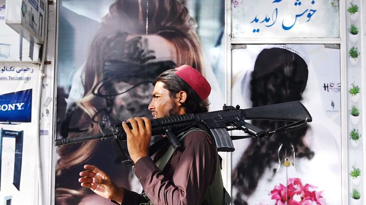 En taliban passerar framför affischer där kvinnoansikten målats över.