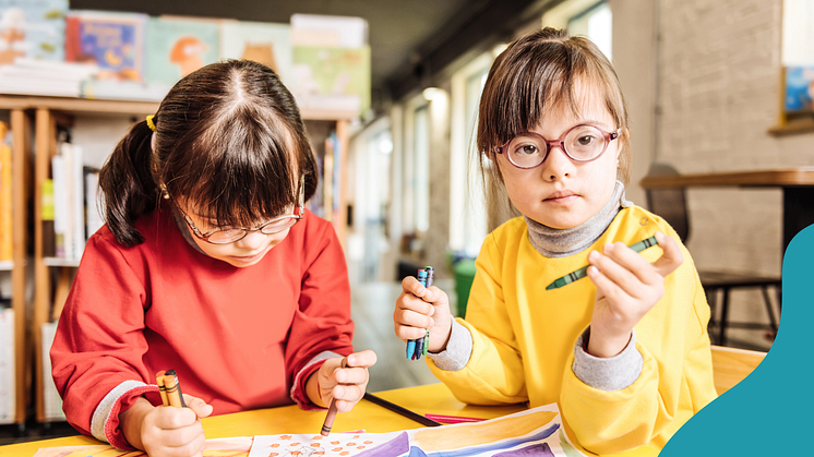 Två barn med Downs syndrom ritar och skriver i skolmiljö