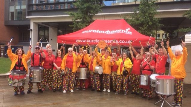 Someone at the Door Samba band playing in Brindley Place with their Cross City Heroes plaque
