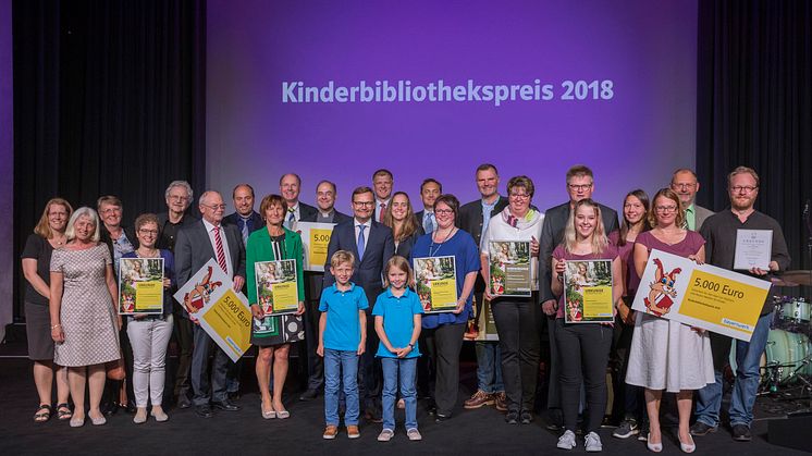 Gemeinsame Preisverleihung, doppelte Freude: Die fünf Gewinner-Büchereien des Kinderbibliothekspreises 2018 strahlen beim Siegerfoto im AURELIUM Lappersdorf mit dem diesjährigen Paul-Maar-Preisträger Jens Raschke (r.) um die Wette.