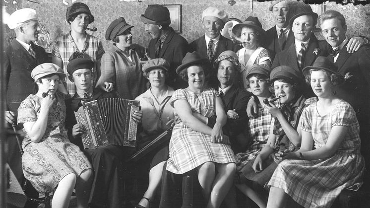 Ungdomsträff vid krutbruket i Åker. Stämningen är uppsluppen. Ungdomarna har bytt hattar med varandra och några av kvinnorna poserar med pipa i munnen. Det är det glada 1920-talet, vilket kan förklara den busiga inramningen. 