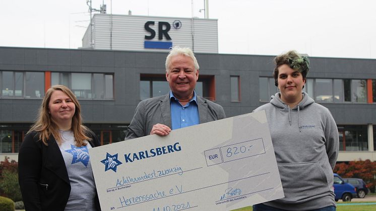 Die Karlsberg-Auszubildenden Melanie Schunk (links) und Leonie Roos (rechts) übergaben den Spendenscheck an Thomas Rosch vom Saarländischen Rundfunk. Foto: Karlsberg