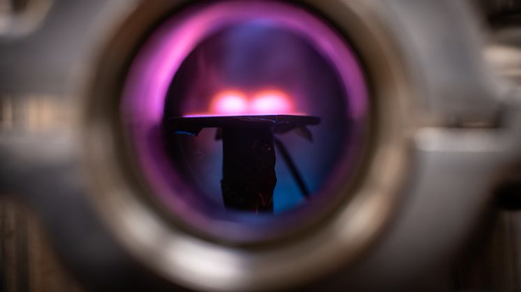 En titt in i vakuumkammaren där man ser plasmat ovanför ytan där metallfilmen skapas.