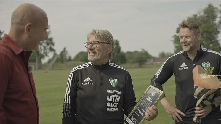 Brålanda IF:s arenaansvarig Bengt Lidre och ordförande Stefan Lindqvist blir glatt överraskade när XL-Hjälpens Hans Fahlén hälsar på och ger vinnarbeskedet.