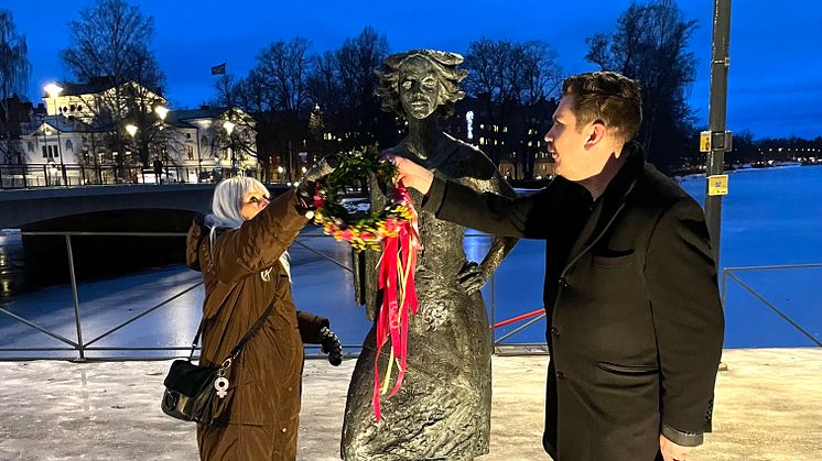 Marianne Nilsson och Robert Halvarsson smyckar skulpturen Sola i Kallsta, av konstnären Herman Reijers, med en blomsterkrans.