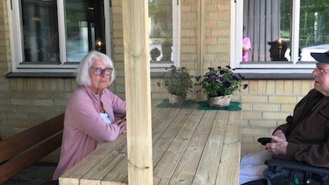 Äkta makarna Birgitta Och Claes Lagerlund vid mötesbänken med plexiglasskiva utanför vård- och omsorgsboendet Ålycke i Johannishus