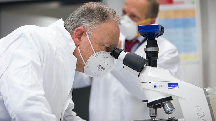 Ministerpräsident Stephan Weil beim Blick durch ein Mikroskop in einem Forschungslabor der DSMZ