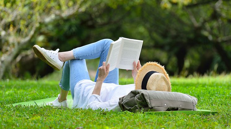 Frau liest auf einem Rasen liegend