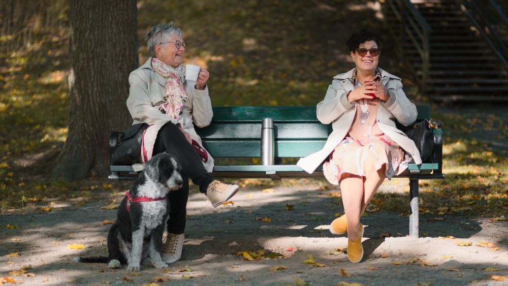 Två kvinnor sitter och pratar på en bänk utomhus