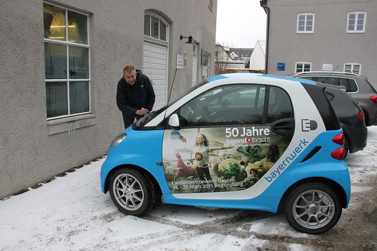 Mit dem „50 Jahre Jugend forscht E-Smart“ trifft das Patenunternehmen Bayernwerk ehemalige bayerische Preisträger, hier Jürgen Geist, und lässt diese das Elektroauto signieren.