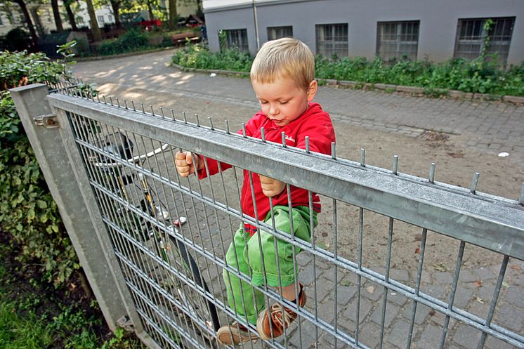 Junge klettert am Gitterzaun, Querformat